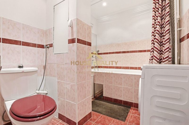A bathroom in a 2-room apartment with a shower, bathtub, and washing machine, featuring red tiles.