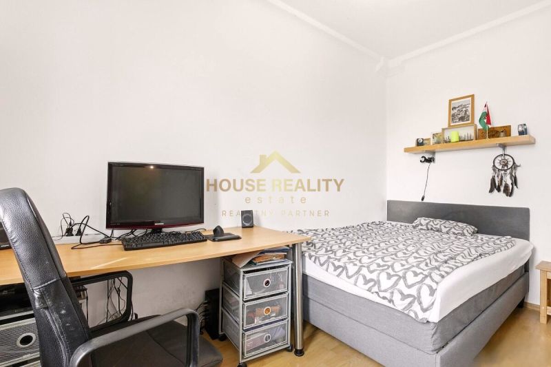 Bedroom in a 2-room apartment with a bed, table, and wooden decor flooring.