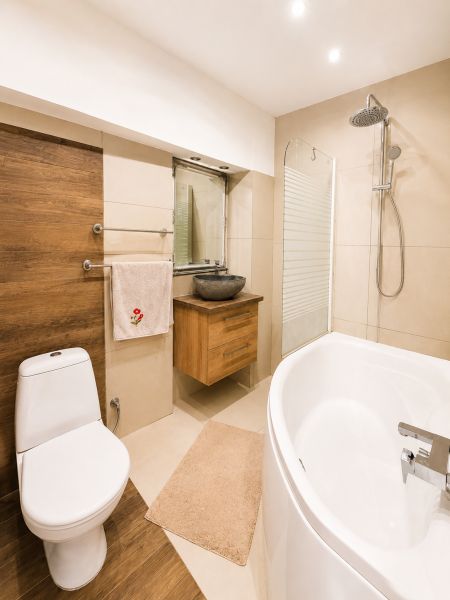 A bathroom in a family house with a corner bathtub and a sink on a wooden decor.