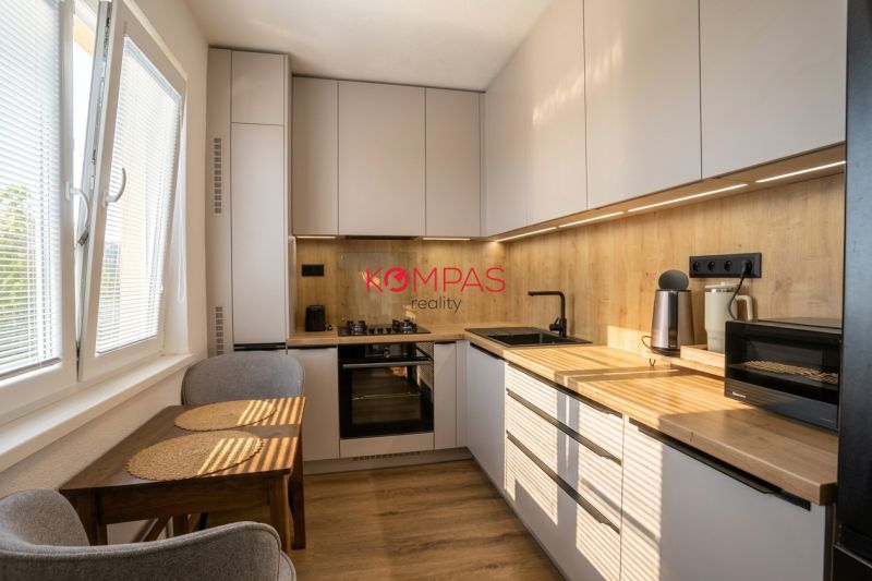 A kitchen in a 2-room apartment with wooden decor cabinets and a compact table.