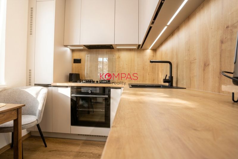 A kitchen in a 2-room apartment with a wooden decor floor, light cabinets, and appliances.
