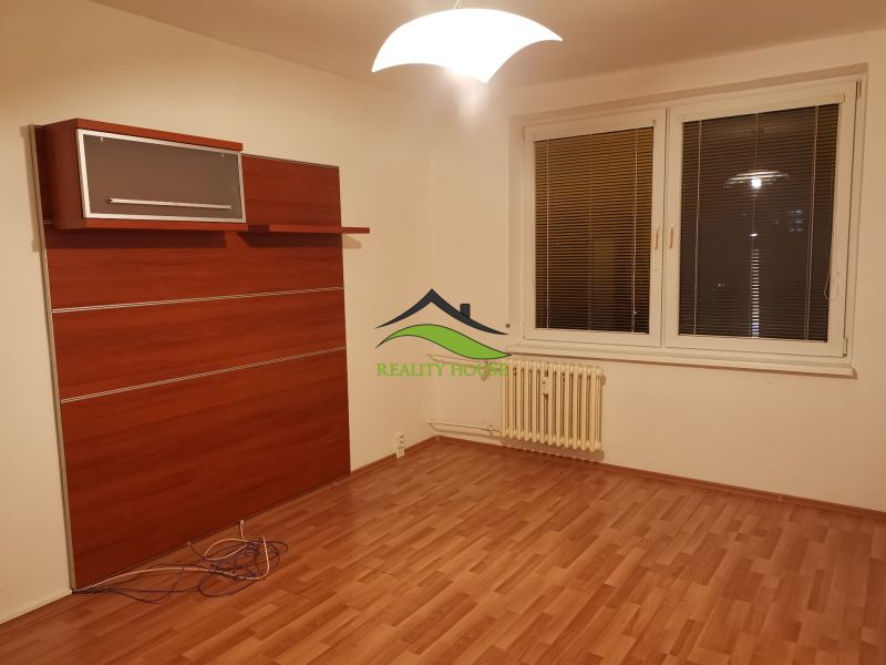 A room with a wooden decor floor, white walls, and a wall cabinet in a 3-room apartment.