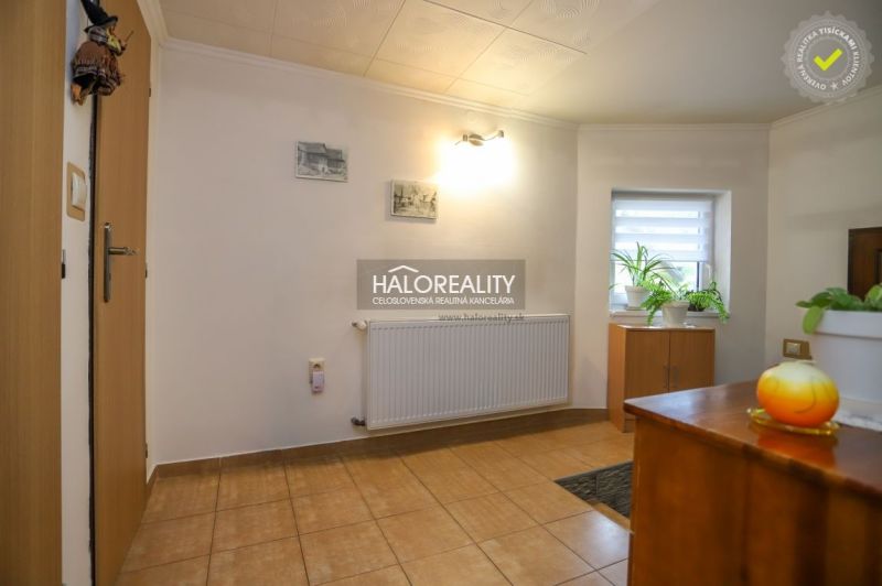 A hallway in a family house with tiles, light walls, plants, and wooden furniture.