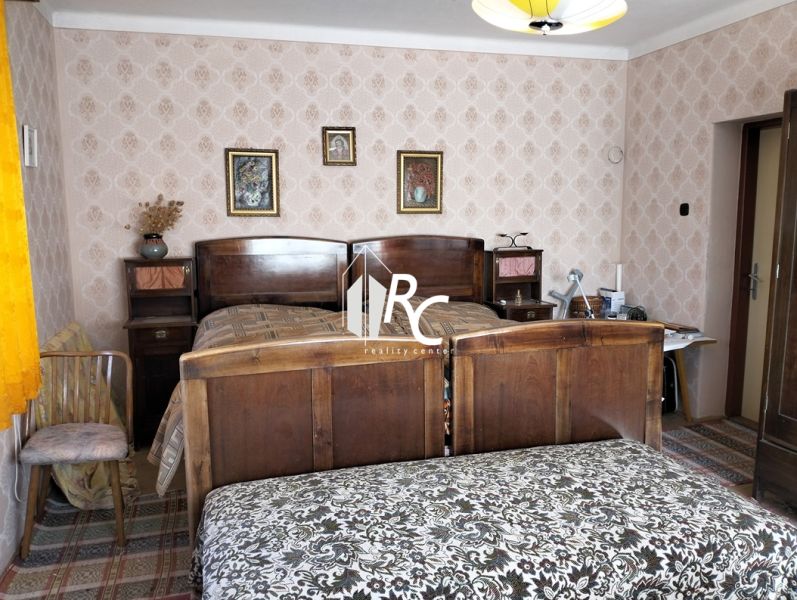 A bedroom in a family house with a wooden bed, patterned wallpaper, and curtains.
