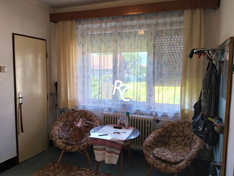 A room in a family house with a table, chairs, and a large window with a view.