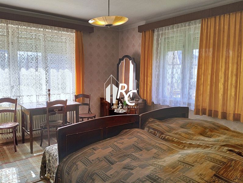 Bedroom in a family house with a bed, table, chairs, and curtains.