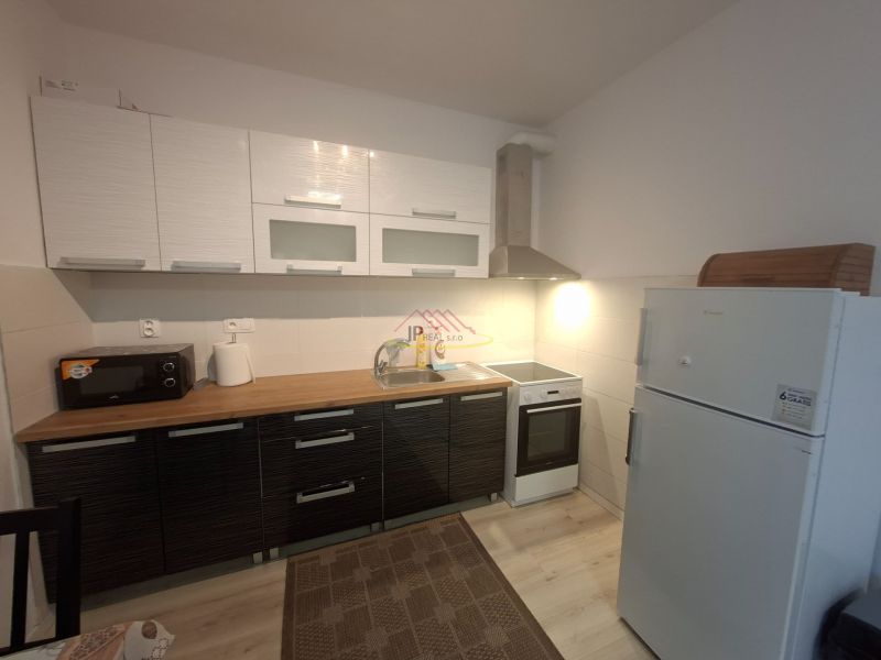A kitchenette in a studio apartment with a countertop, microwave, sink, and refrigerator, with a wooden decor floor.