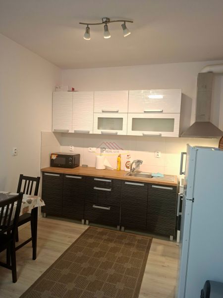 Kitchen unit in a studio apartment with cabinets, dining table, wooden decor flooring.