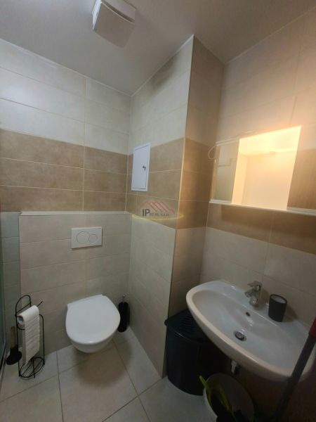 A bathroom in a studio apartment with a sink, toilet, and walls tiled.
