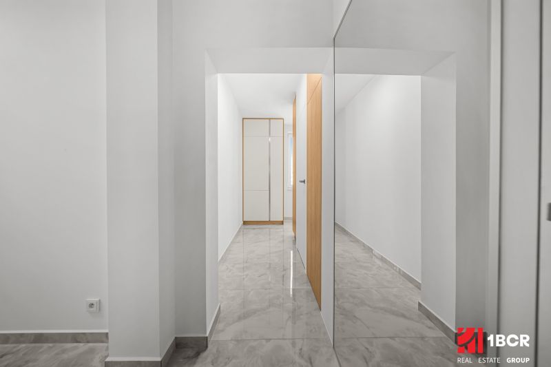 A hallway in a 3-room apartment with a large mirror, light-colored walls, and tiles.