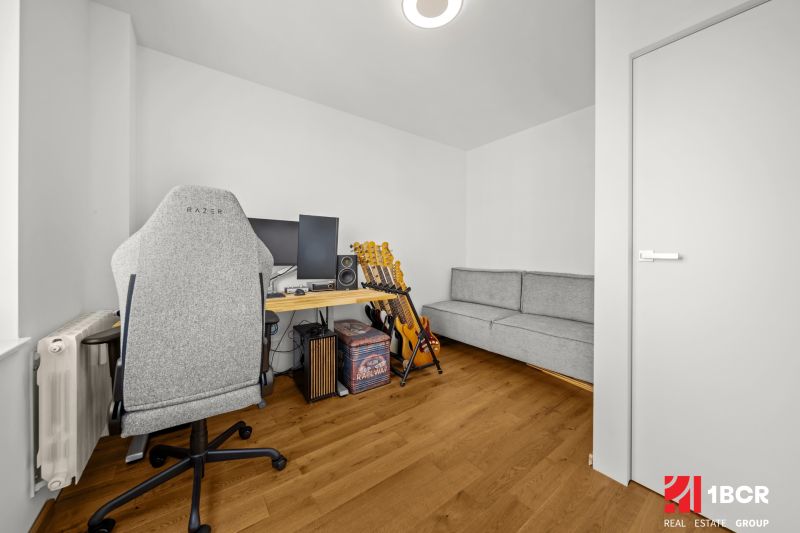 A study with a computer, guitars, a gray chair, and a wooden decor floor in a 3-room apartment.