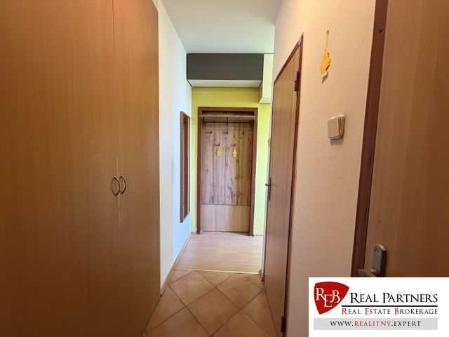 A hallway with a wardrobe and a coat rack in a studio apartment with tiles and wooden decor.