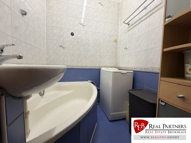 A bathroom in a studio apartment with a bathtub and a washing machine, tiled with white and blue tiles.
