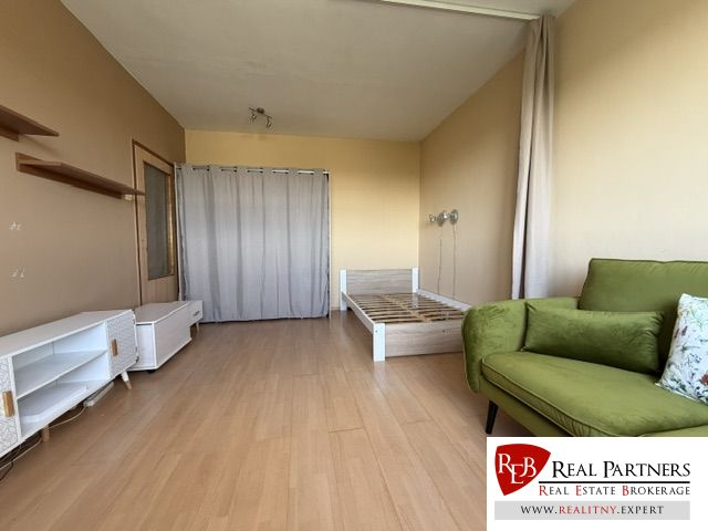 A room in a one-room apartment with a wooden decor floor, a bed, and a green sofa.