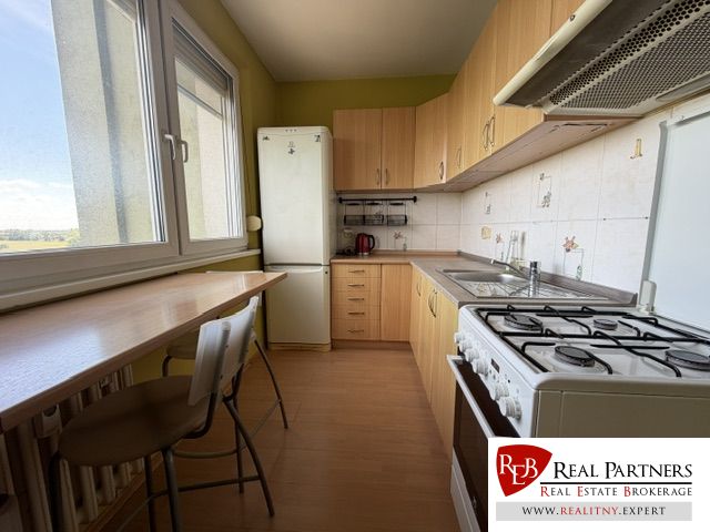 A kitchen in a studio apartment with a wood-patterned floor and light-colored furniture.