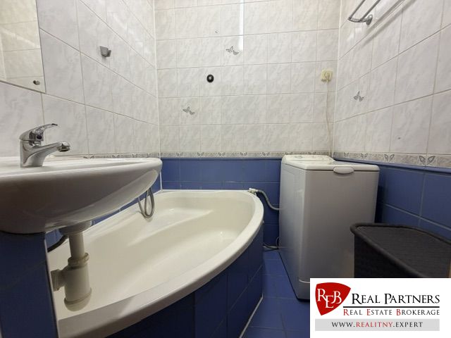 Bathroom in a studio apartment with a shower, sink, washing machine, and blue tiles.
