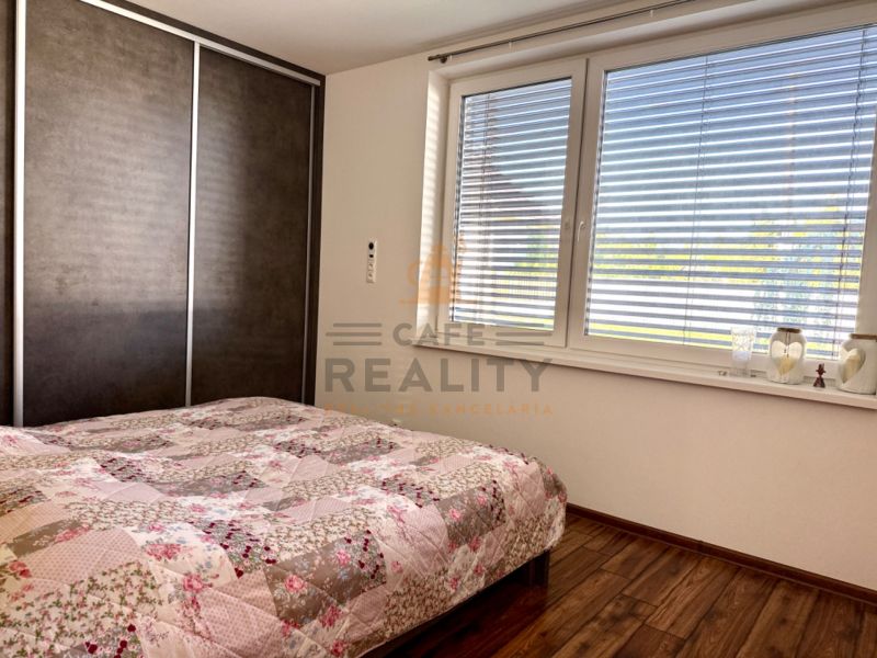 A bedroom in a family house with a large window, a bed, and a floor with a wooden decor.