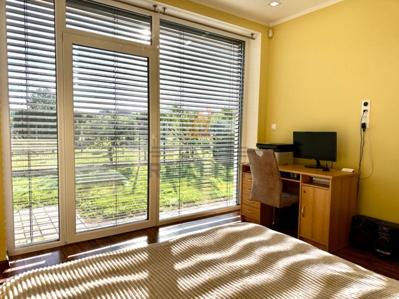 A room in a family house with large windows, blinds, a table, and a computer.