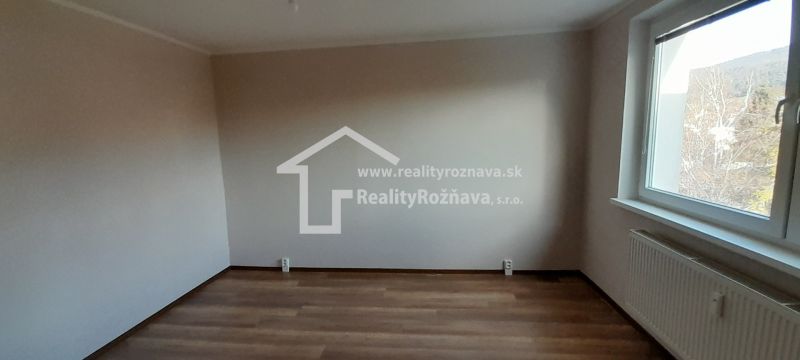 A room in a 2-room apartment with a wood-patterned floor and a large window.