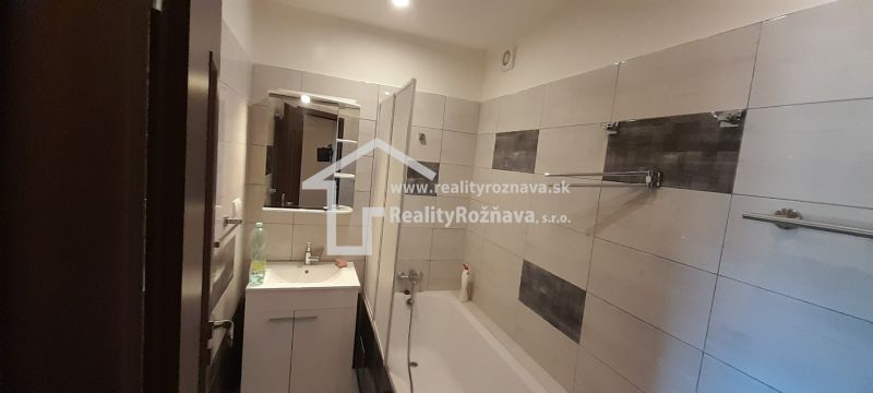 A bathroom with a bathtub and a sink in a 2-room apartment, tiled with light tiles.
