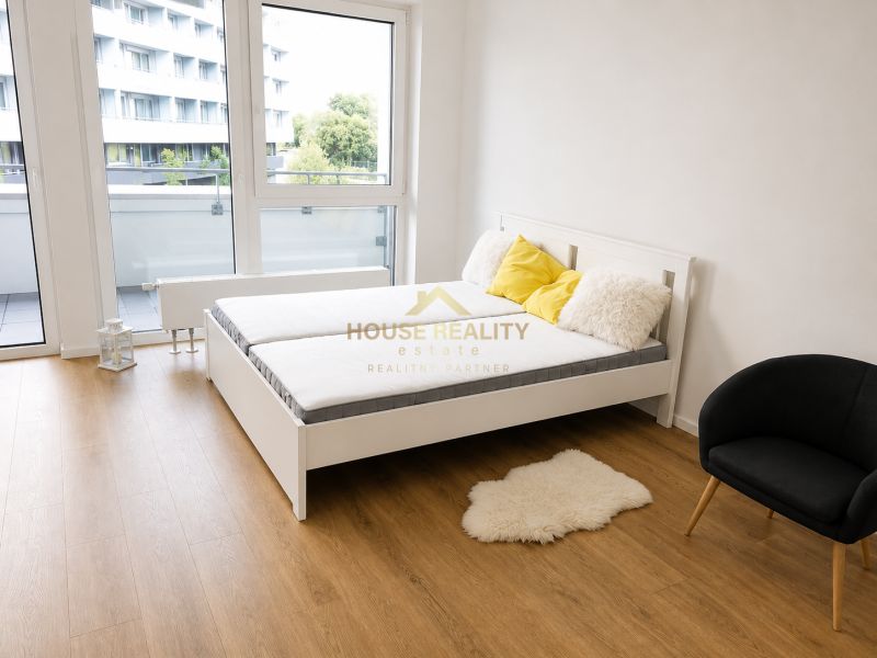 A one-bedroom apartment with a bed, an armchair, a wooden floor, and balcony doors.