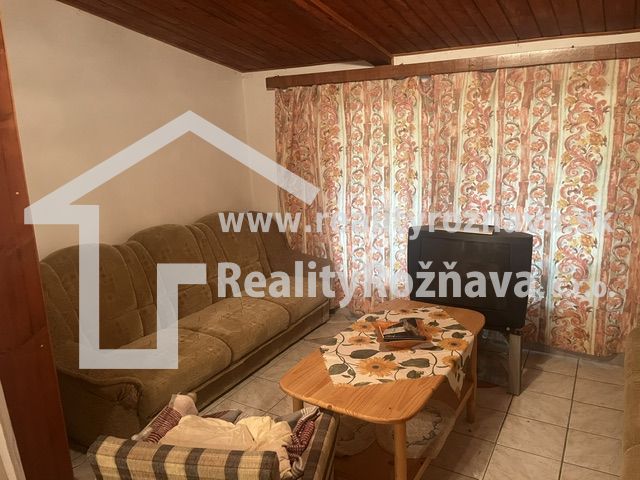Living room in a cabin with a sofa, armchair, television, and floral curtain.