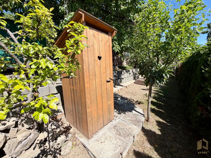 A wooden latrine near a cottage in Kunov, Senica, surrounded by greenery and trees.