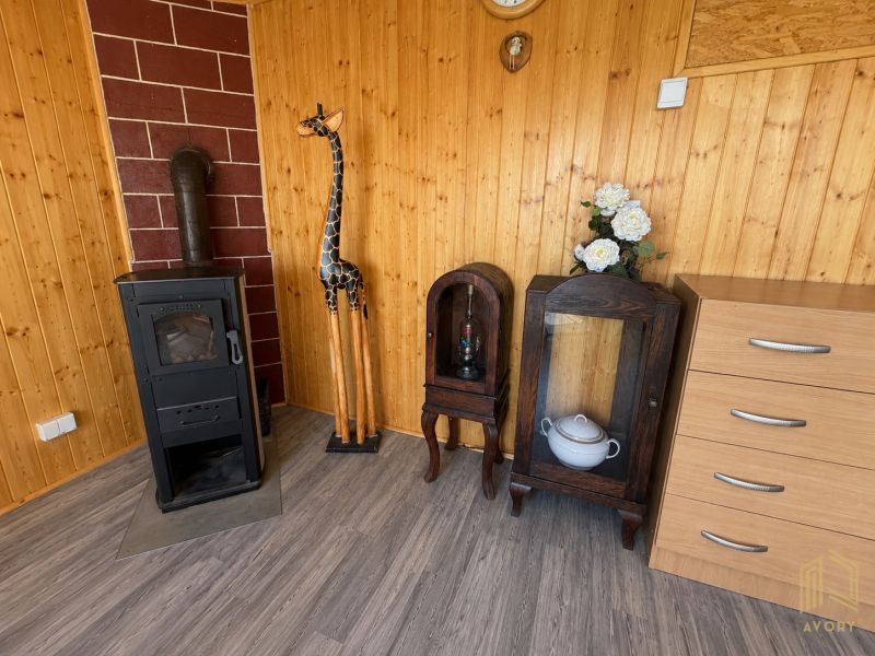 A wooden interior of a cabin with a stove, a giraffe, and furniture on a floor with a wooden decor.