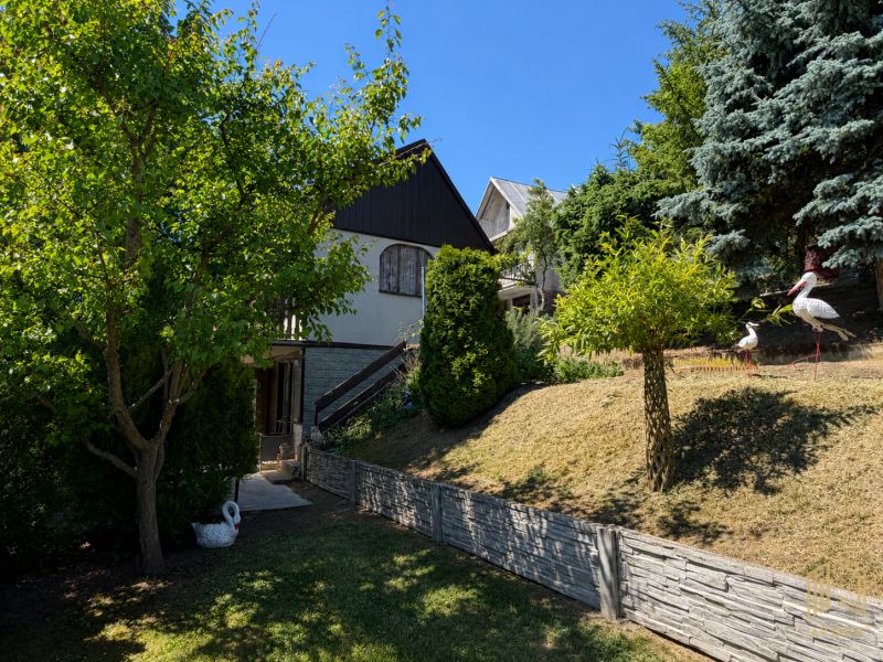 A cottage in Kunov, Senica, surrounded by trees and a garden with stork statues.