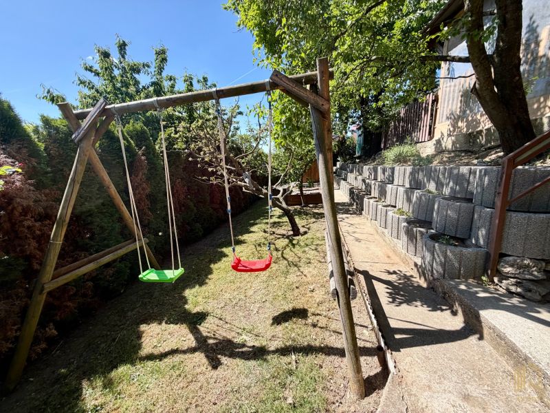 Wooden swings in the yard of the cottage in Kunovo, Senica, with a terraced garden layout.
