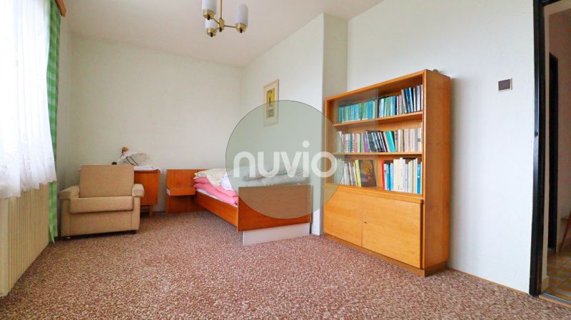 A room in a family house with a chair, a bed, a shelf, and a colorful carpet.
