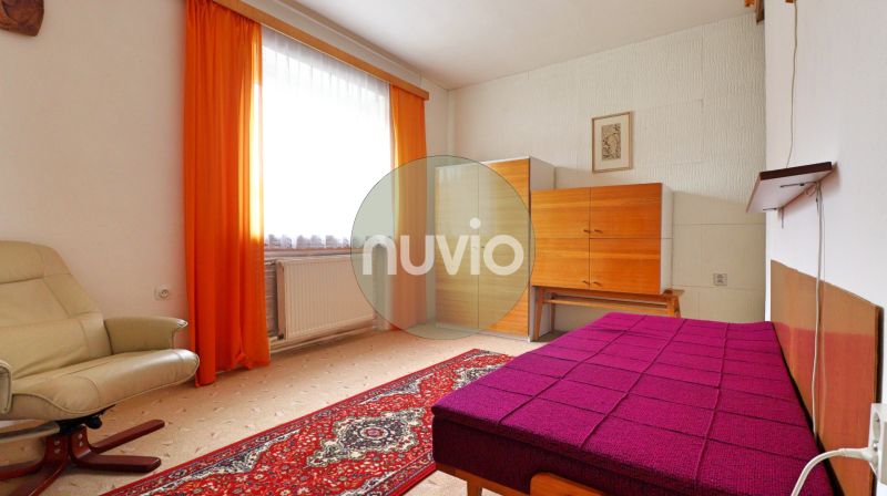 A room in a family house with a light armchair, furniture, and striking orange curtains.