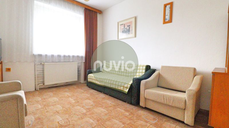 Living room with a sofa, an armchair, paintings on the wall, and a floor with a wooden decor.