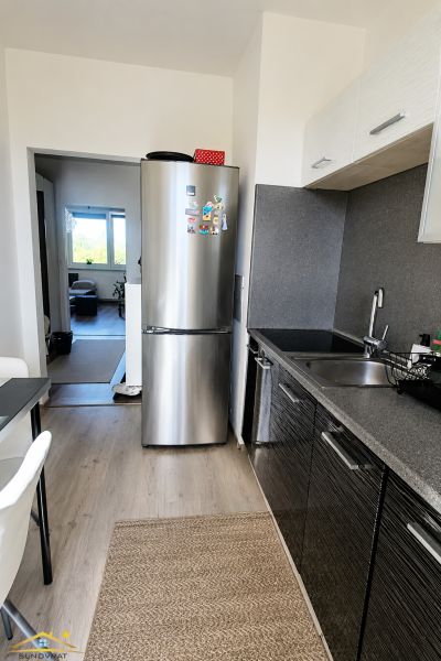 A kitchen in a 2-room apartment with a refrigerator and a floor with a wooden decor.