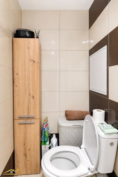 Toilet in a 2-room apartment with a storage cabinet, bin, and cleaning supplies.