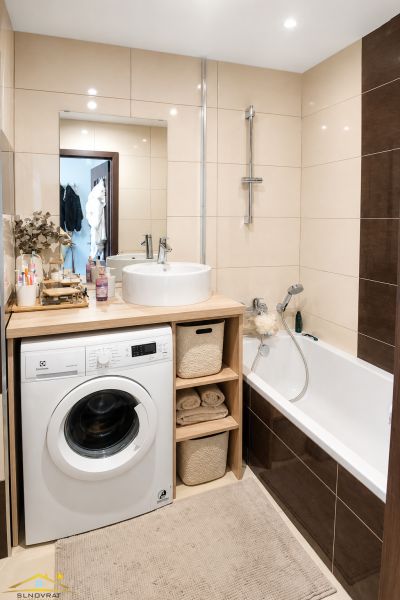Bathroom in a 2-room apartment with a sink, washing machine, and bathtub, beige tiles.