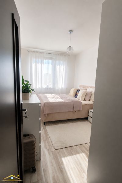 A bright bedroom with a bed and wood-patterned flooring in a 2-room apartment.