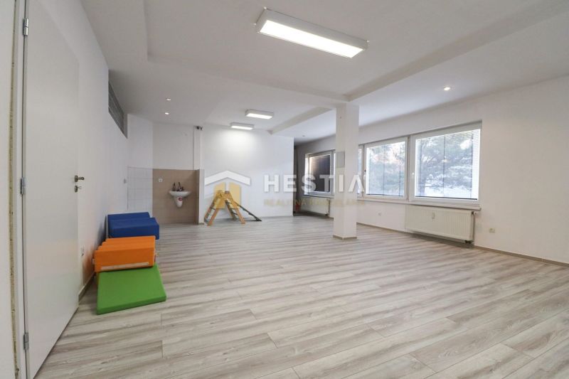 Interior of commercial spaces with wood-patterned flooring, light walls, and large windows.