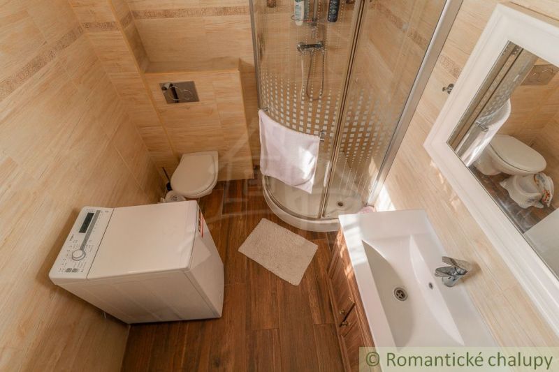 Bathroom with a washing machine, shower, and wooden decor flooring in a family house.