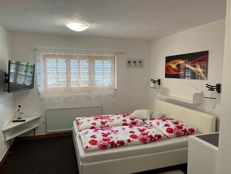 A bedroom in a family house with white walls, a bed, and a television on the wall.