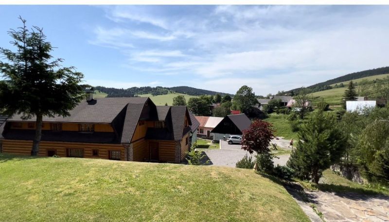 Family houses in Veľké Borové with lawns and hilly landscape in the background.