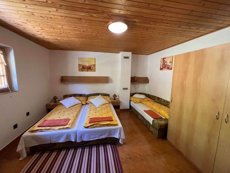A bedroom with a wooden ceiling, three beds, and a floor with a wooden decor in a family house.