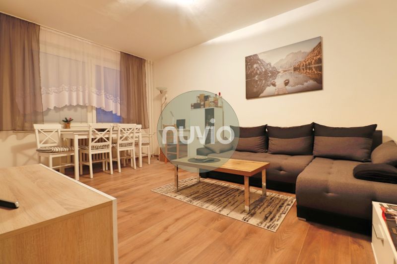 Living room with a dark sofa, dining table, and wooden decor flooring in a two-room apartment.