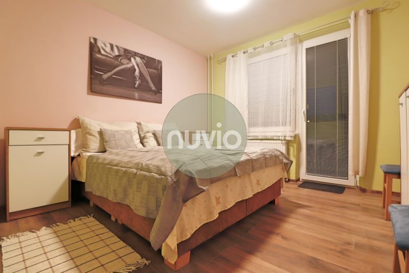 Bedroom in a two-room apartment with a bed, a painting, and a wooden decor floor.