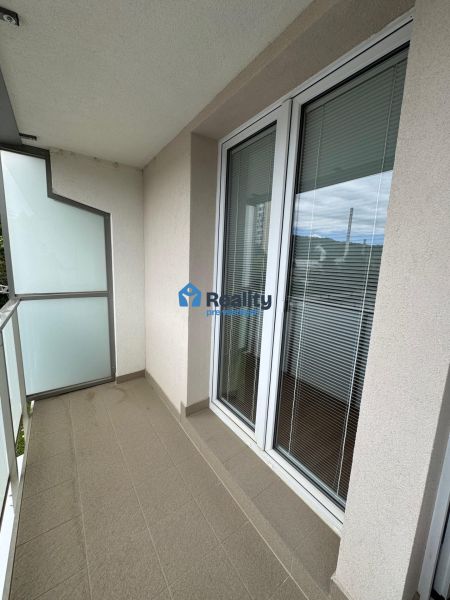 Balcony of a 2-room apartment with a tiled floor, railing, and glass doors.