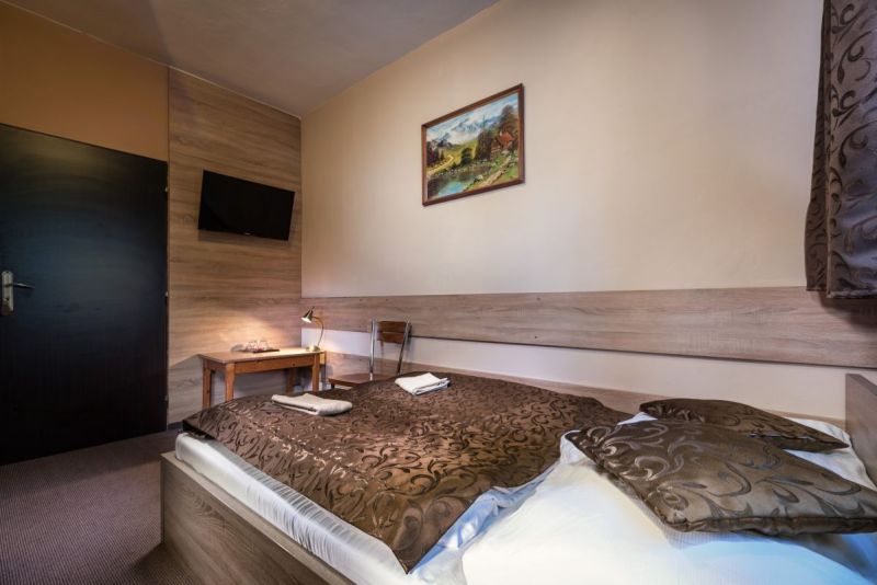 A hotel room interior with a bed, decorative blanket, and a TV on the wall.
