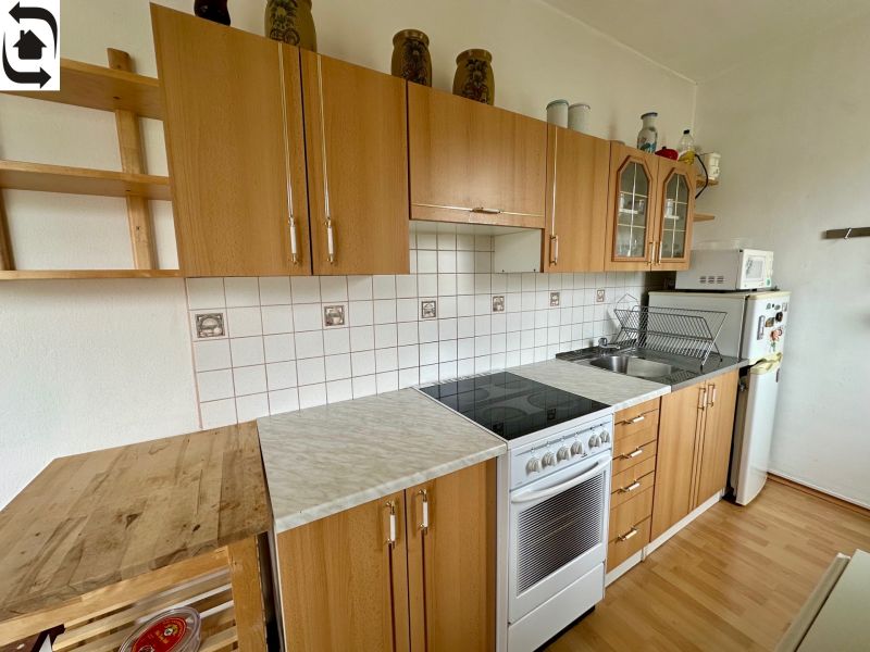 Kitchen in a studio apartment with wood decor flooring, light cabinets, ceramic tiles.