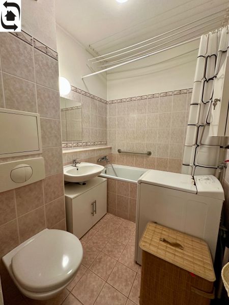 A bathroom in a one-room apartment with a bathtub, washing machine, and sink, tiled with tiles.