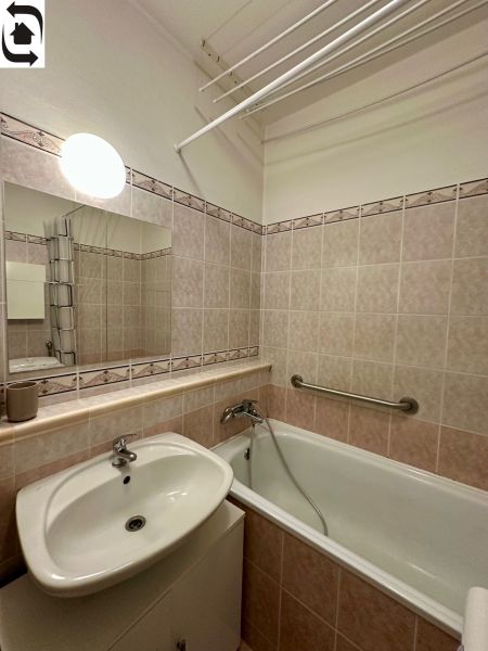 A bathroom in a studio apartment with a bathtub, a sink, and tiles in light shades.