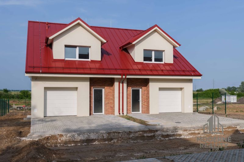 A family house in Andovce with a red roof and a garage, with landscaped terrain in front of the house.